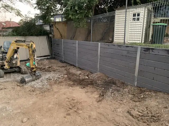 Excavator preparing the ground beside a new concrete sleeper wall