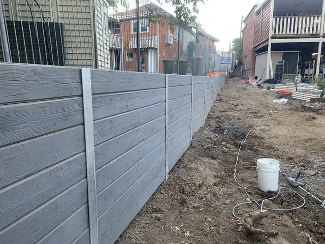 Grey timber-look concrete sleeper retaining wall along a laneway boundary