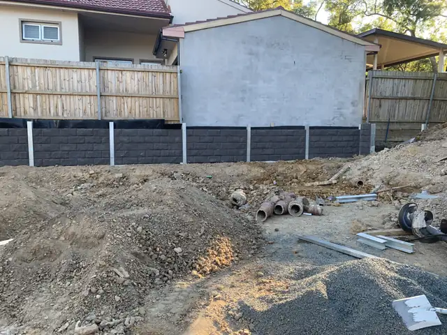 Long charcoal concrete sleeper retaining wall along a timber fence in a Sydney backyard