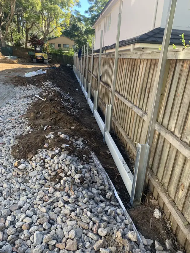 Gravel drainage backfill behind a new sleeper retaining wall along a fence