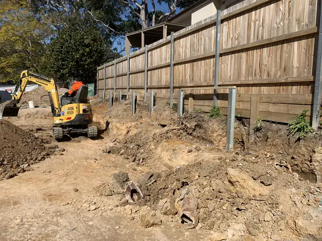 Excavator and steel posts set out for a new retaining wall on a sloping site