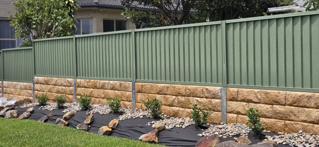 Sandstone-look concrete sleeper wall under a green Colorbond fence with new garden bed