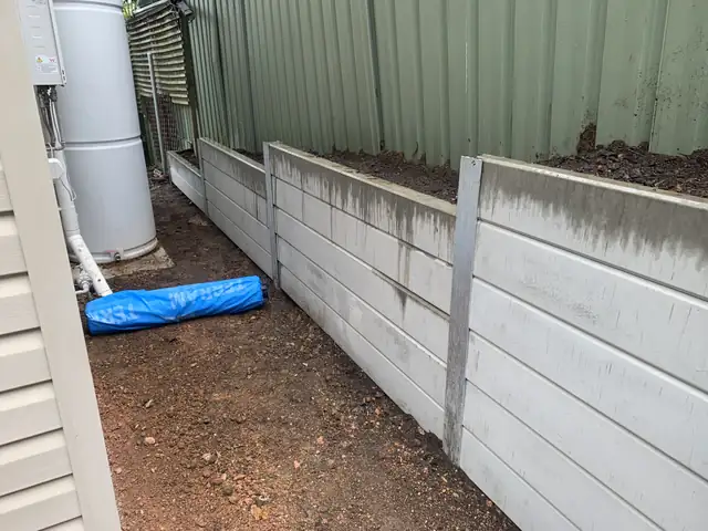 White concrete sleeper retaining wall with galvanised posts beside a Colorbond fence