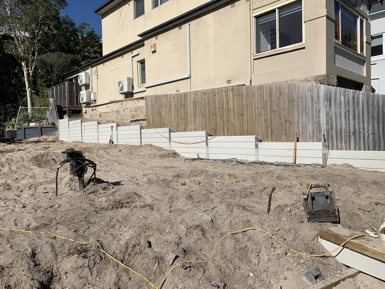 White concrete sleeper retaining wall on a sloping site with house behind